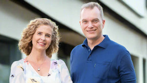 Smiling man in blue polo and woman in floral dress standing outdoors near modern building