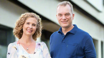Smiling man in blue polo and woman in floral dress standing outdoors near modern building