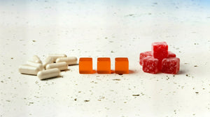 Comparison of white supplement capsules, orange lozenges, and red gummy candies on a white surface.