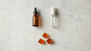 Amber dropper bottle, clear spray bottle, and three orange botanical lozenges on white marble.