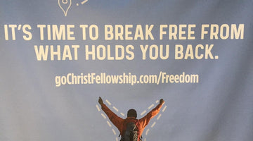 Man in orange jacket cheering atop a peak with 'FREEDOM' text and inspirational quote.