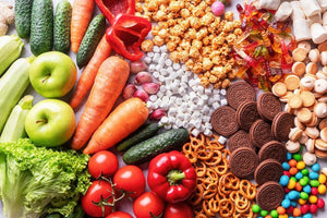 Fresh vegetables and fruits with candy, popcorn, cookies, gummy bears, and pretzels arranged side by side