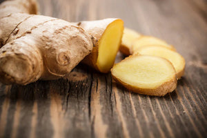 Fresh whole ginger root and sliced ginger pieces on a rustic wooden surface