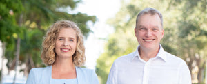 Tracy and Dean smiling together outdoors against a blurred greenery background.