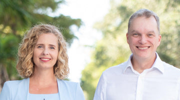 Tracy and Dean smiling together outdoors against a blurred greenery background.