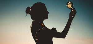 Silhouette of a woman holding a glowing light bulb against a twilight sky