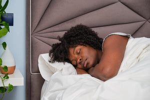 A Black woman sleeping peacefully in a bed with a grey tufted headboard.