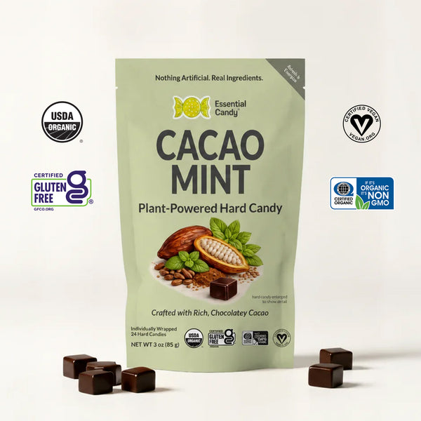 A stand-up pouch of Essential Candy Cacao Mint plant-powered hard candy, shown on a clean white background with several chocolate mint candies placed in front. The package is light sage green with black and yellow text, and several certification logos appear around it.