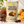 Load image into Gallery viewer, A stand-up pouch of Essential Candy Cacao Orange hard candy is centered on a light stone surface, surrounded by oranges, cocoa beans, chocolate pieces, and leaves. The package is cream-colored with large black text and fruit imagery, and the scene is styled to emphasize the orange-cacao flavor.
