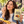Load image into Gallery viewer, A woman outdoors holds a bag of Essential Candy Cacao Orange plant-powered hard candy while eating a chocolate-covered orange piece. The bag is beige with bold black and orange text, and the scene includes sliced oranges and chocolate pieces on a wooden surface.

