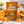 Load image into Gallery viewer, A bag of Essential Candy Orange Cinnamon plant-powered hard candy stands on a kitchen counter surrounded by oranges, cinnamon sticks, and several translucent orange candy pieces. The package is brown-orange with white text and fruit illustrations.
