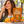 Load image into Gallery viewer, A woman outdoors bites a piece of hard candy while standing beside a stand displaying a bag of Essential Candy Orange Cinnamon plant-powered hard candy, with oranges, cinnamon sticks, and citrus slices arranged around it.
