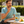 Load image into Gallery viewer, A man in a light blue t-shirt sits at an outdoor wooden table, eating a yellow candy from his hand while a box of 'Peppermint Mandarin' gummy candies sits on the table next to fresh mandarins.
